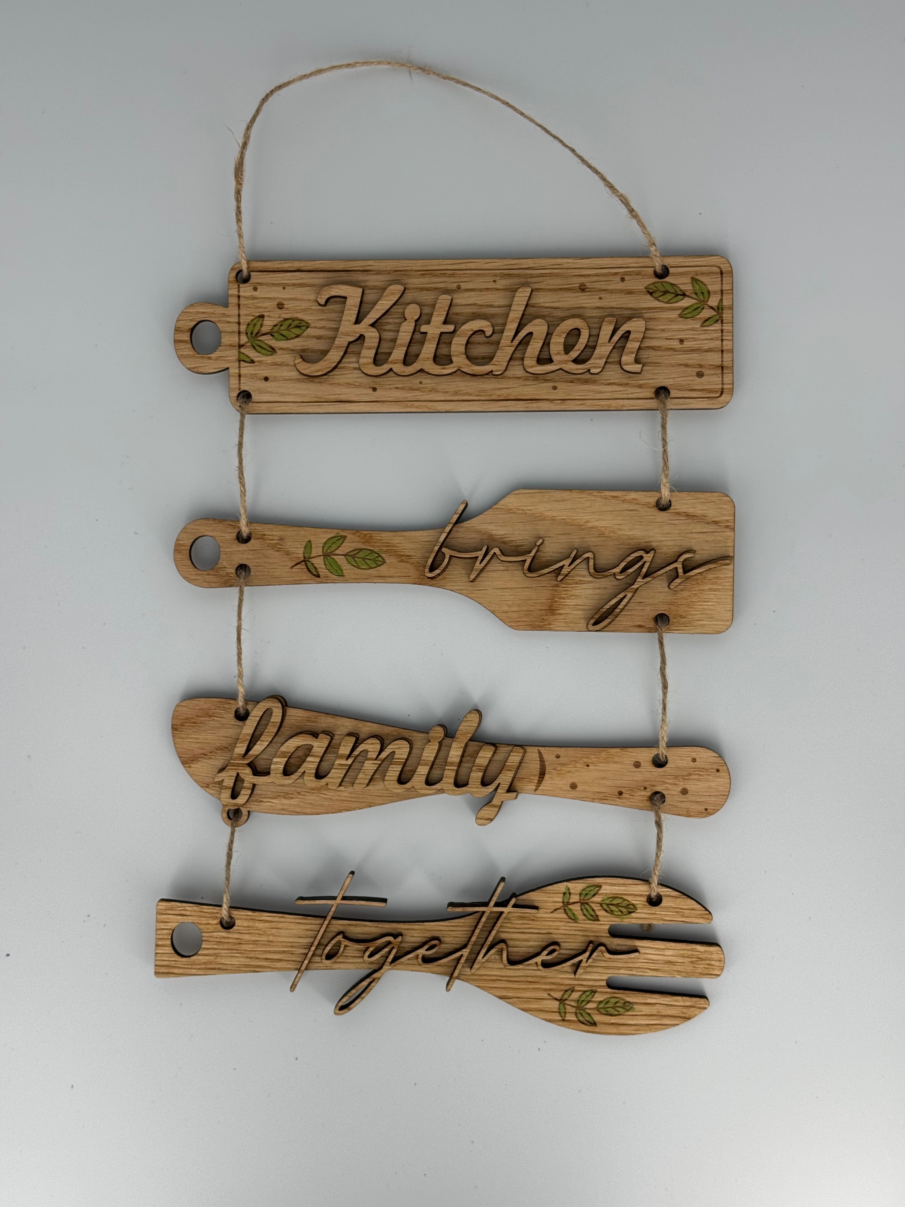 Wooden kitchen utensil wall hanging with laser-engraved text reading Kitchen brings family together