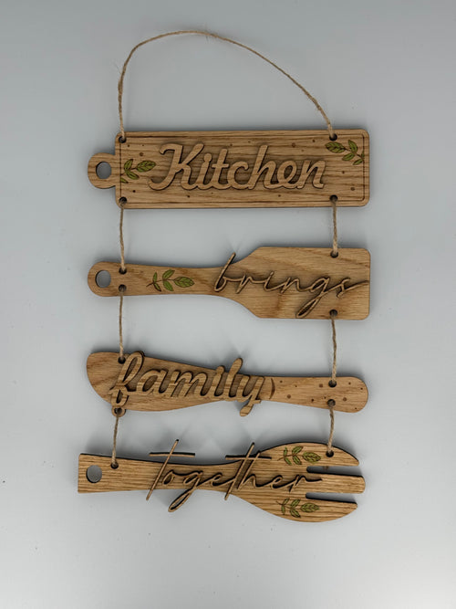 Wooden kitchen utensil wall hanging with laser-engraved text reading Kitchen brings family together
